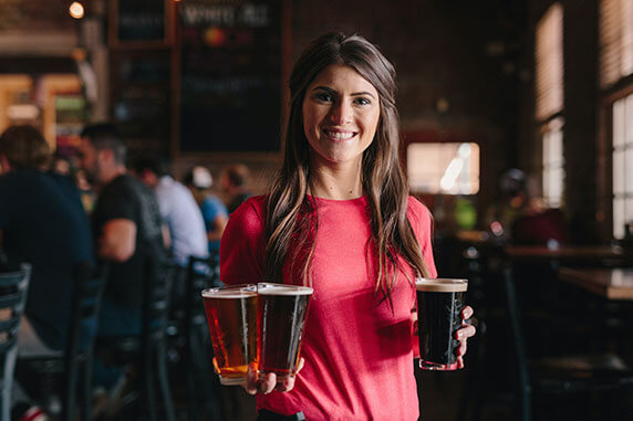 A woman smiling holding three beers in her hands